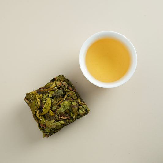 Floral Zhangping Shuixian tea cake with brewed tea liquor in a white cup