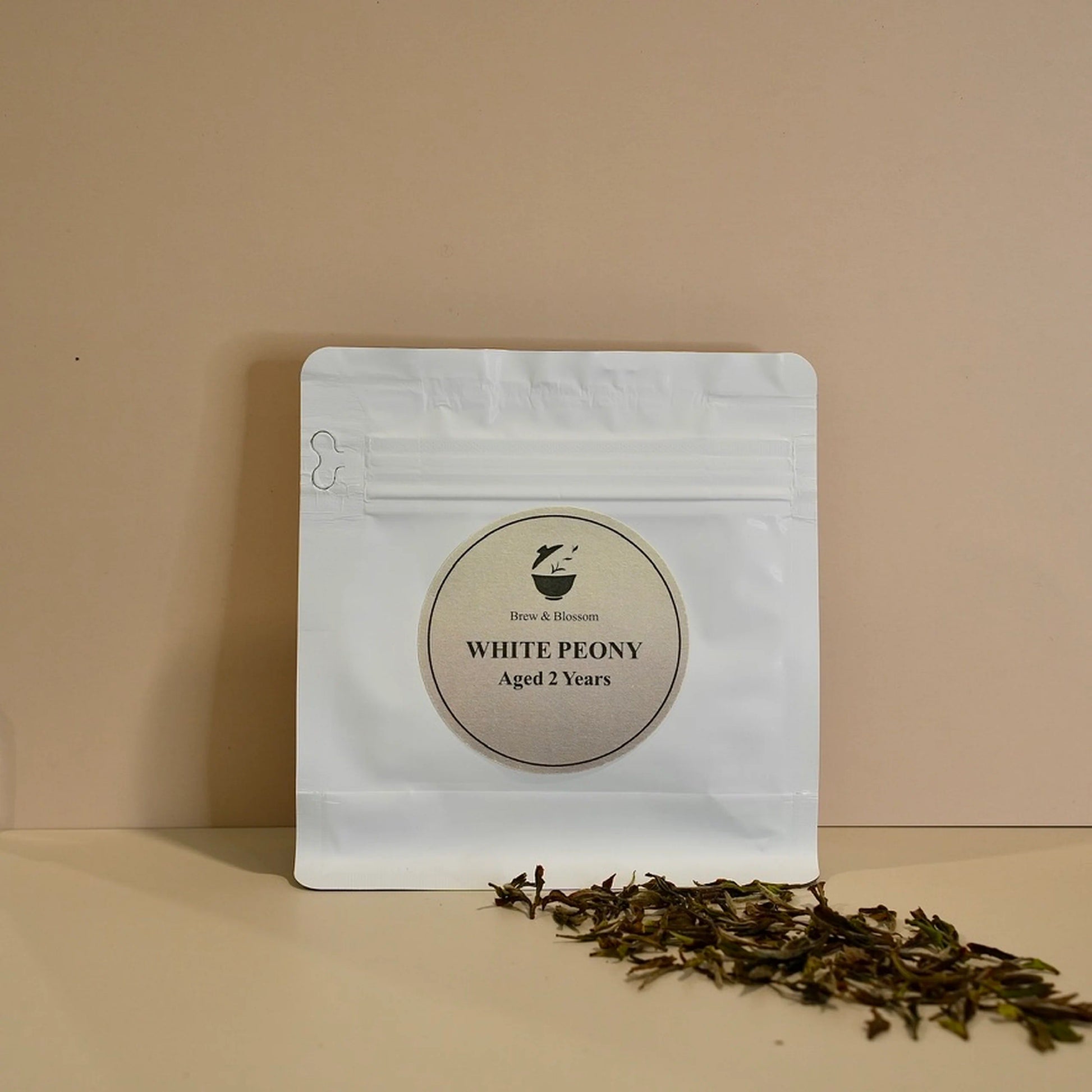 White Peony tea pouch with loose-leaf white tea in front