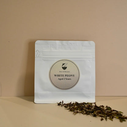White Peony tea pouch with loose-leaf white tea in front